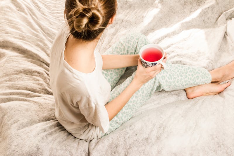 Aerial View Photography of Woman Sitting on Blanket While Holding Mug Filled With Pink Liquid Looking Sideward