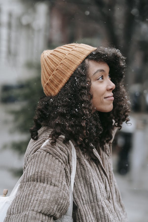A young woman with curly hair and warm clothing enjoying a snowy day in the city.