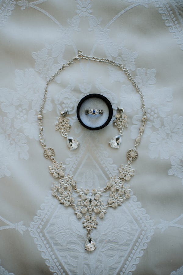 A beautiful flat lay of a jewelry set including necklace, earrings, and ring on a lace background.