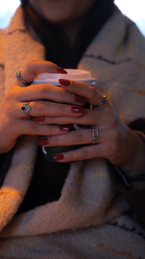 Close-up of a woman's hands holding a hot coffee cup, wrapped in a blanket.
