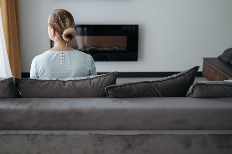 Rear view of a woman sitting alone on a couch, reflecting in a modern living room setting.