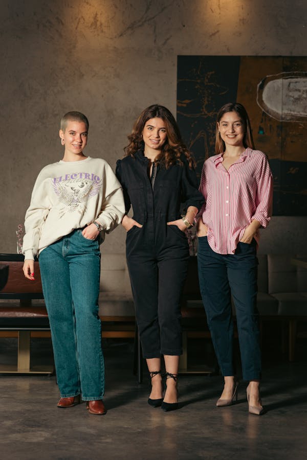 Three young women posing confidently in a studio. Fashionable outfits and relaxed expressions.