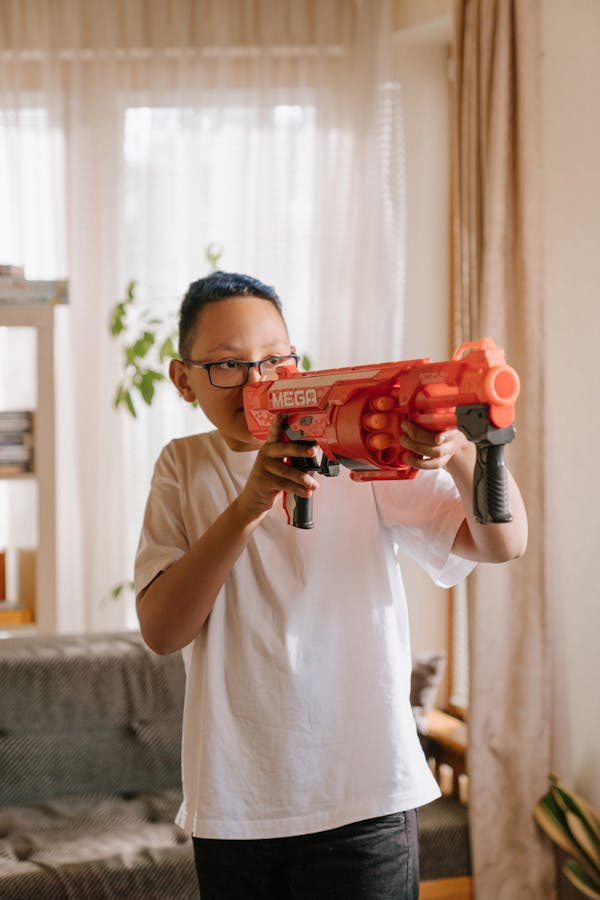 A young boy with glasses having fun playing with a toy water gun indoors.