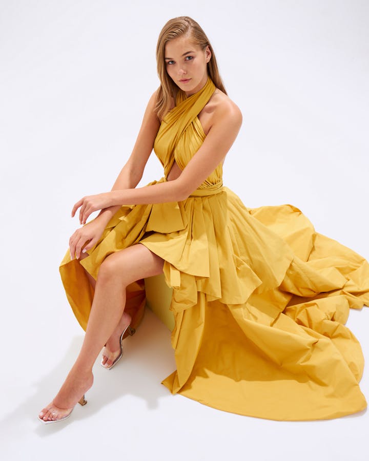 Caucasian woman in a flowing yellow dress sitting elegantly for a fashion portrait.