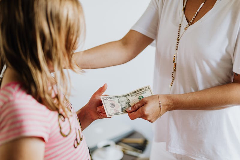 The Fashionable Housewife's Guide to UGMA Accounts A woman handing money to a young girl, symbolizing family financial education and transactions.