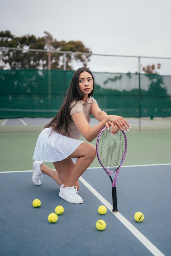 Brunette woman posing with tennis racket on outdoor court.