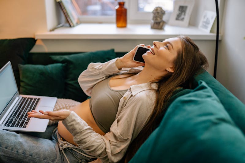 Expecting mother relaxing on a couch with a laptop, enjoying a phone call. smart tools for moms