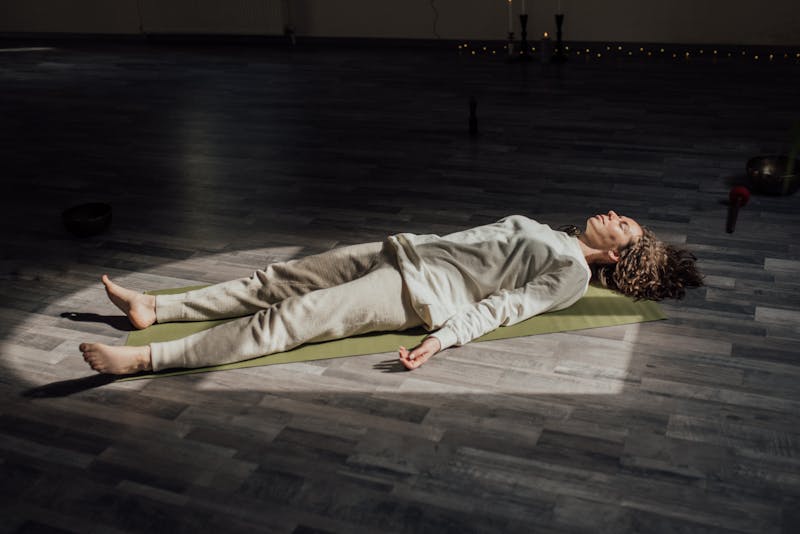 wellness trends Woman lying on a yoga mat indoors, meditating and relaxing in a calm setting.