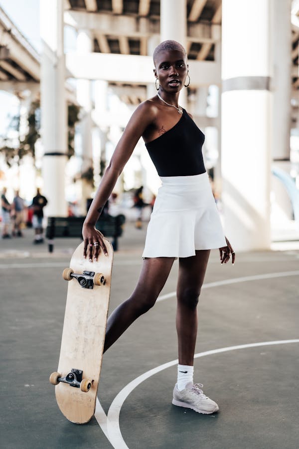 Young woman with hoop earrings and skateboard, standing confidently on outdoor court.