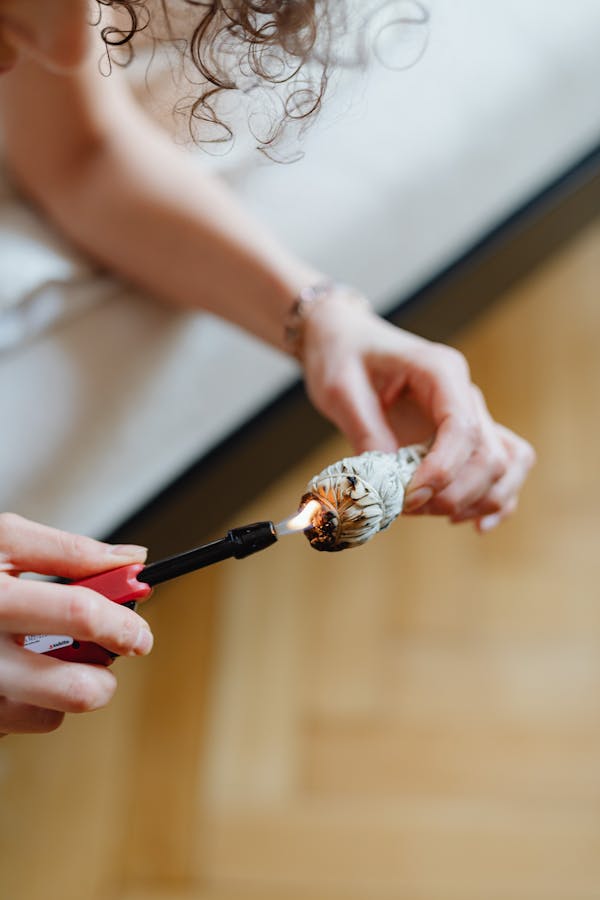 Close-up of a woman burning sage with a lighter, indoors.