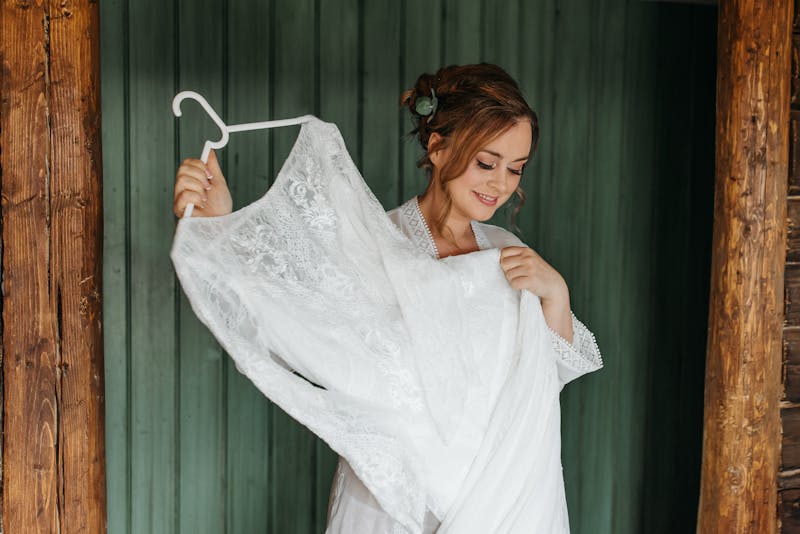 Bride smiling while holding her wedding dress on hanger indoors.