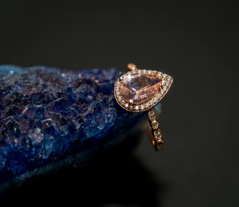 Close-up of a luxurious rose gold ring with a tear-shaped gemstone on a vibrant blue geode.