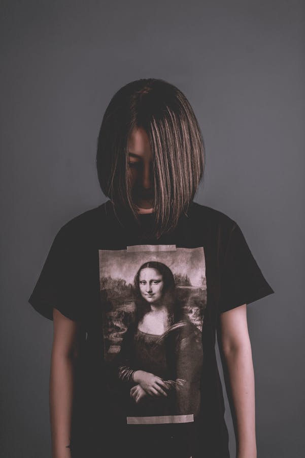 A woman in a dark T-shirt featuring the Mona Lisa stands against a neutral background.
