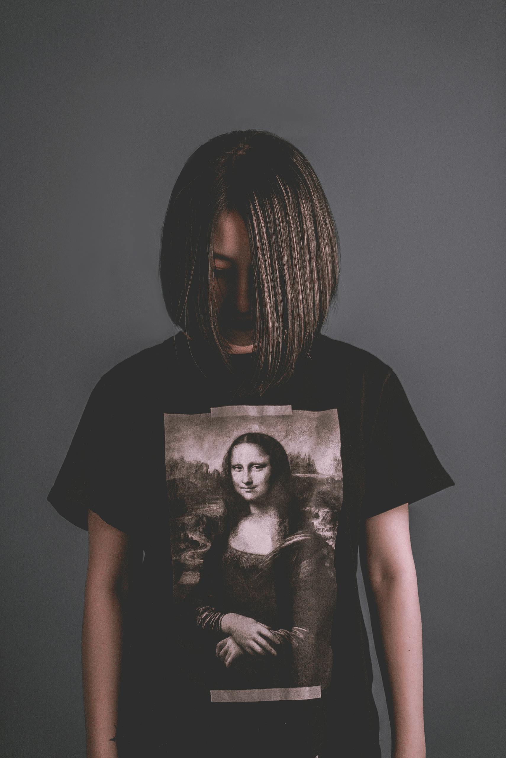 A woman in a dark T-shirt featuring the Mona Lisa stands against a neutral background.