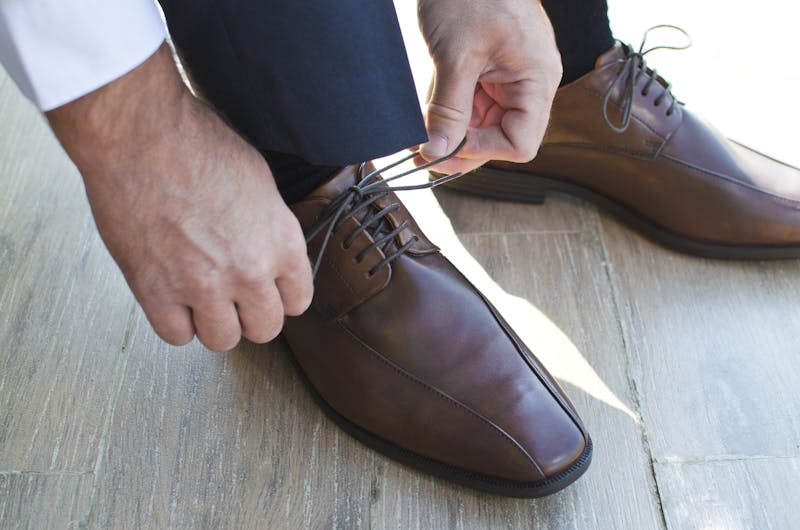 Close-up of a man tying elegant brown leather shoes on a wooden floor.