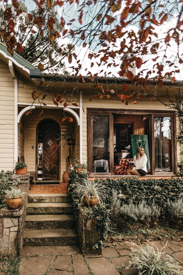 Charming bungalow with person relaxing on porch, surrounded by autumn leaves and greenery.