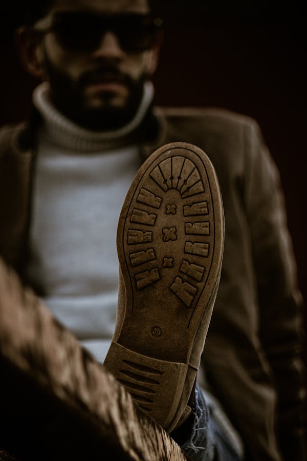 Close-up of a man's boot sole with a fashionable outfit in the background, captured outdoors.