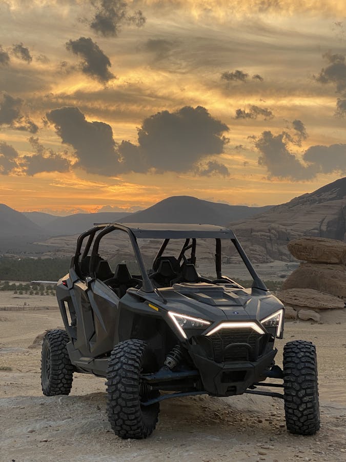 An off-road vehicle parked against a stunning sunset backdrop in a desert landscape.