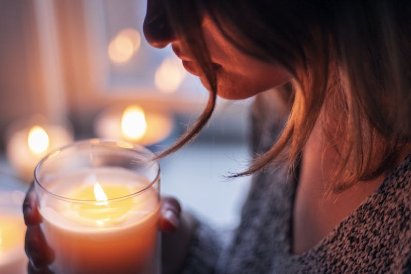 A woman embraces warmth and tranquility while holding a glowing candle indoors.