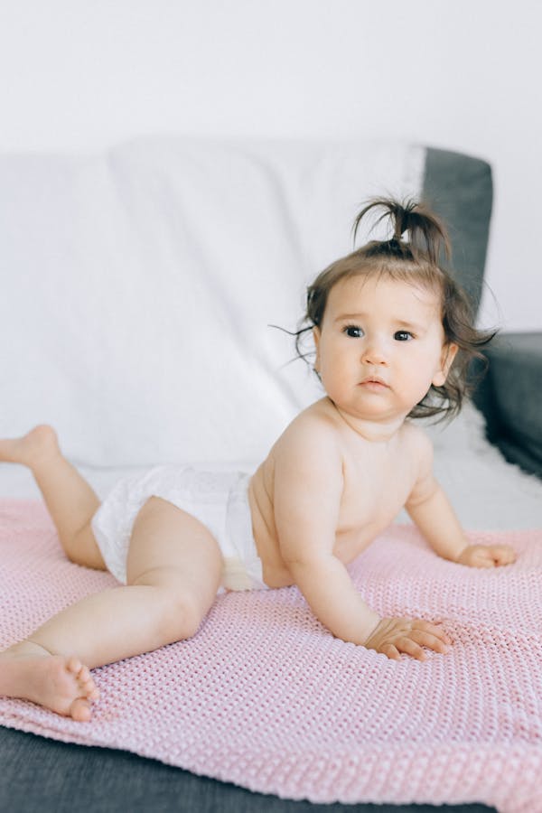 Charming baby in a diaper on a soft pink blanket indoors, looking curious.