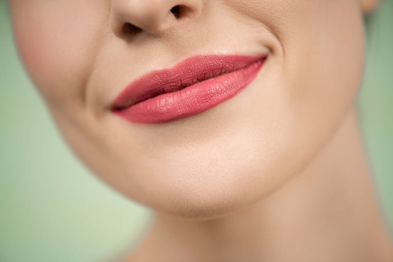 A detailed close-up of a woman's smile with pink lipstick on a green background.