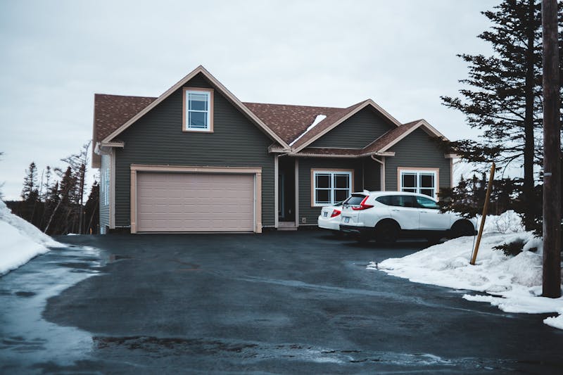 A suburban house with snow-covered surroundings and a parked car during winter.