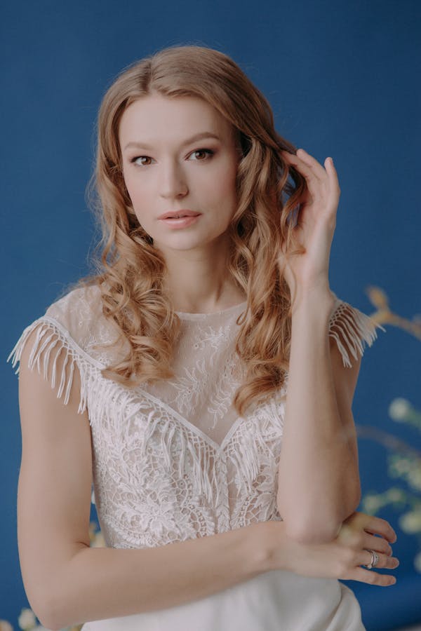 Stunning portrait of a woman in a white lace dress against a blue background.