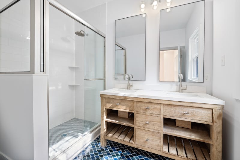 Bright and airy bathroom featuring dual mirrors and a wooden vanity with modern fixtures.