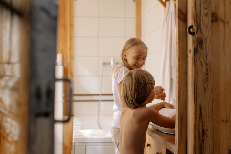Two children washing hands in a rustic bathroom, promoting hygiene and cleanliness.